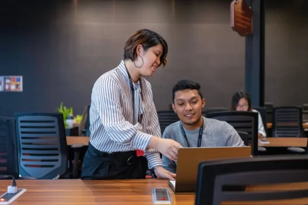 klg-hotdesk-2 Person giving guidance to another in hot desk/open office area